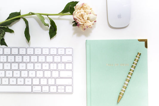 Flat lay of a laptop, coffee, journal, and smartphone on a clean desk—symbolizing a modern millennial woman building a faceless online business.